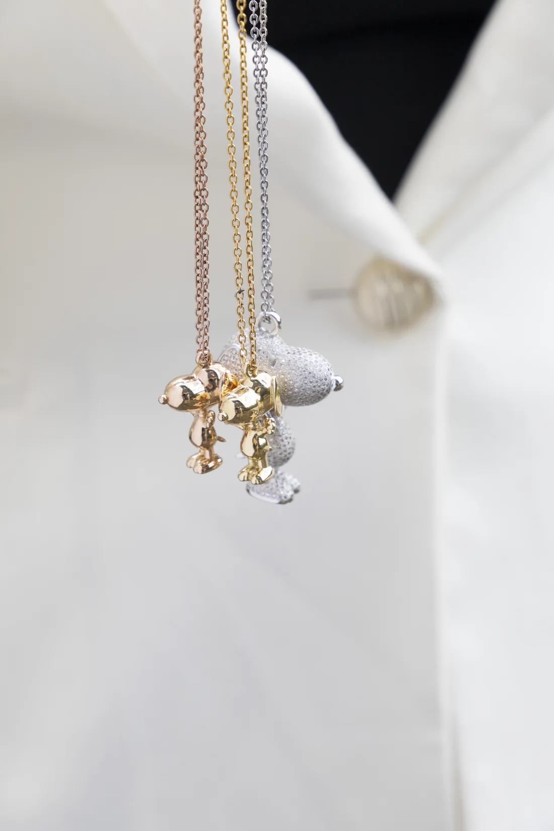 Rose, white, and yellow gold Snoopy pendants hanging together on a white shirt