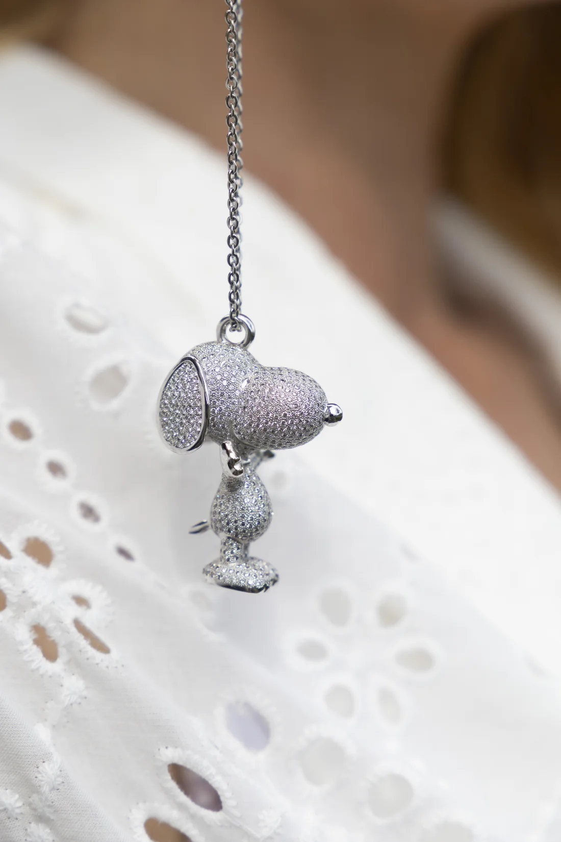 The diamond Snoopy pendant worn on a white eyelet blouse