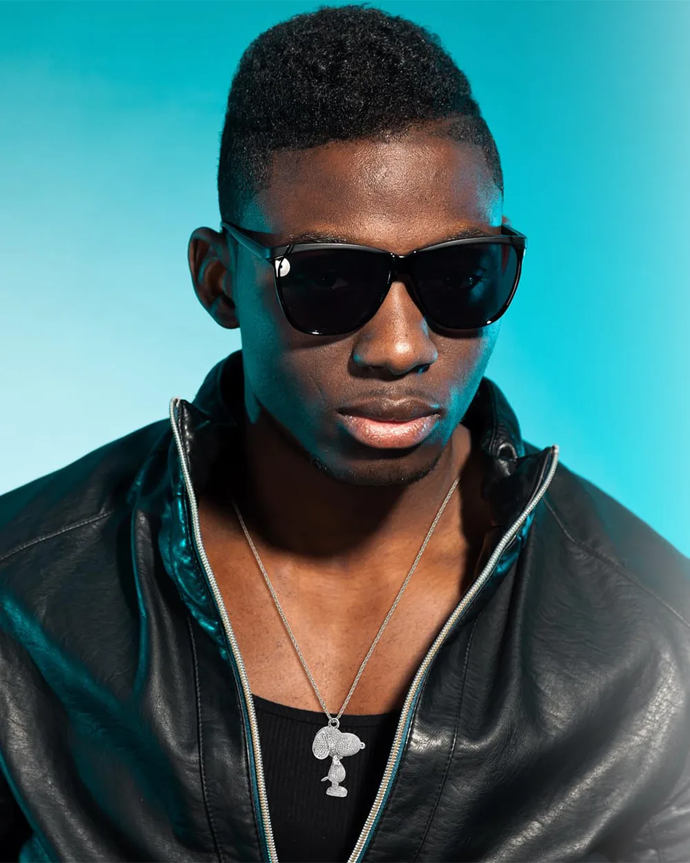 Launch editorial graphic: a model in sunglasses and a leather jacket wearing the Snoopy pendant on a teal backdrop