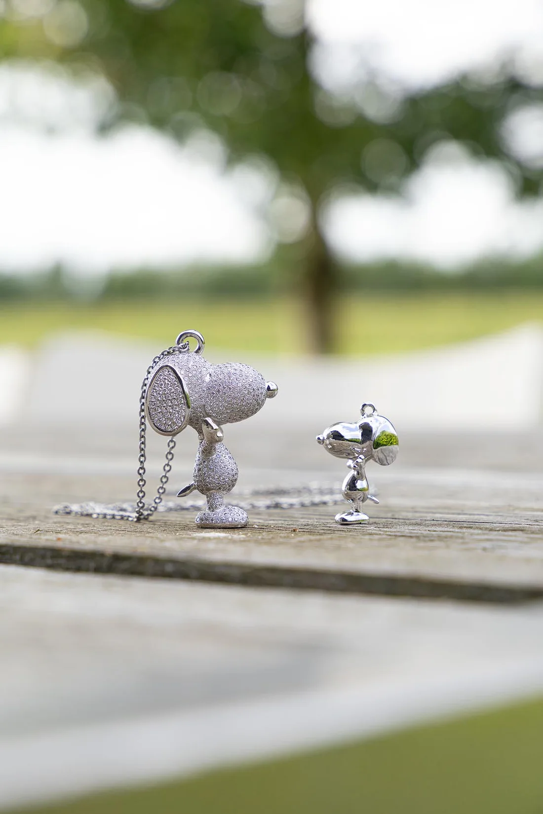 The pave diamond Snoopy pendant beside the polished 18k companion piece