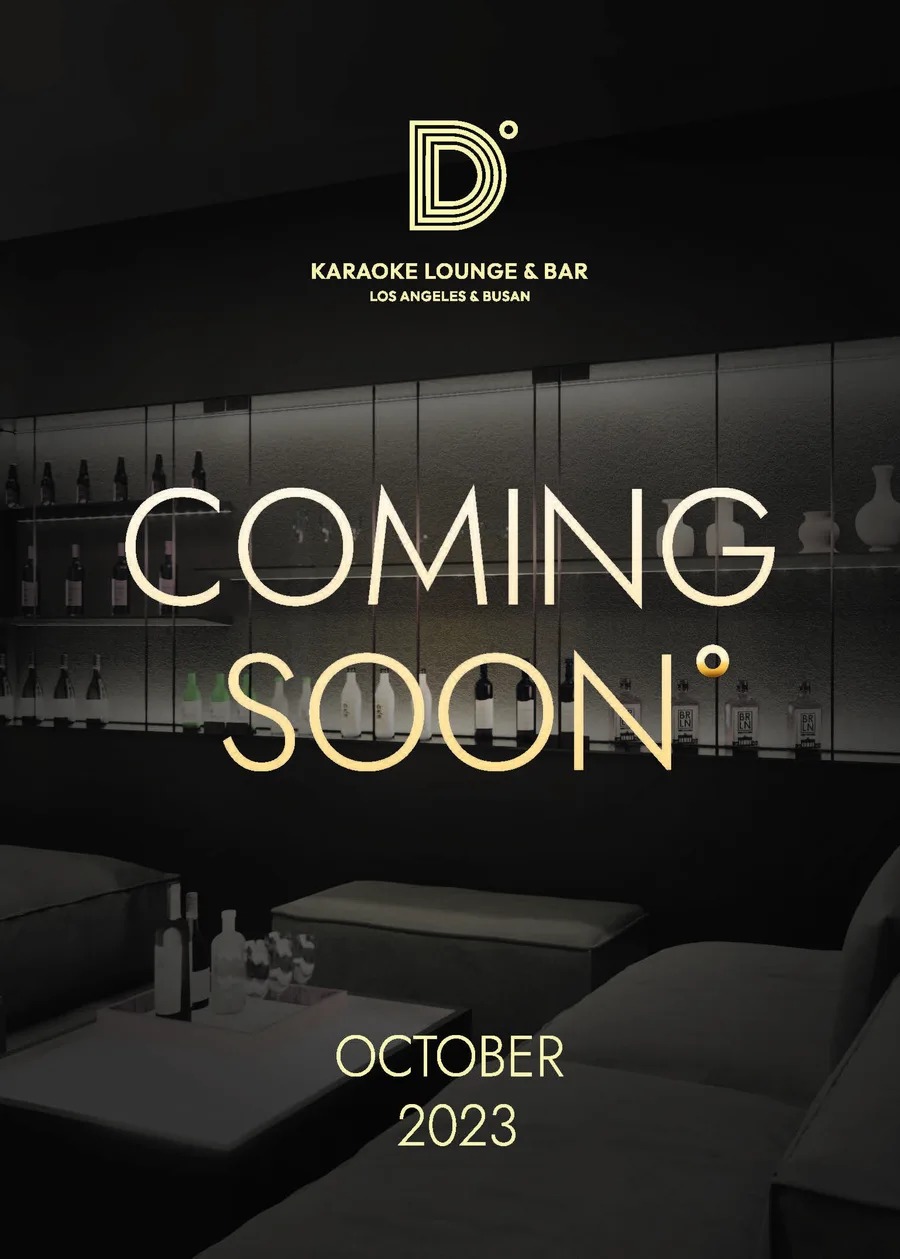 The gold-on-black D Lounge karaoke bar coming-soon table banner, Los Angeles and Busan