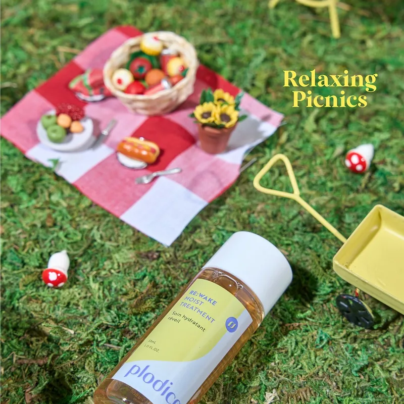 Miniature picnic blanket with tiny food beside a Plodica bottle